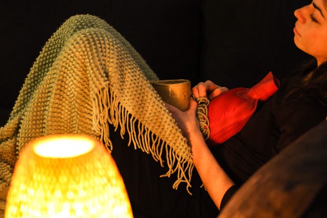 <p>This illustration photograph taken on 1 March 2023 shows a woman with painful periods lying on a sofa while holding a hot water bottle in Toulouse, southwestern France</p>